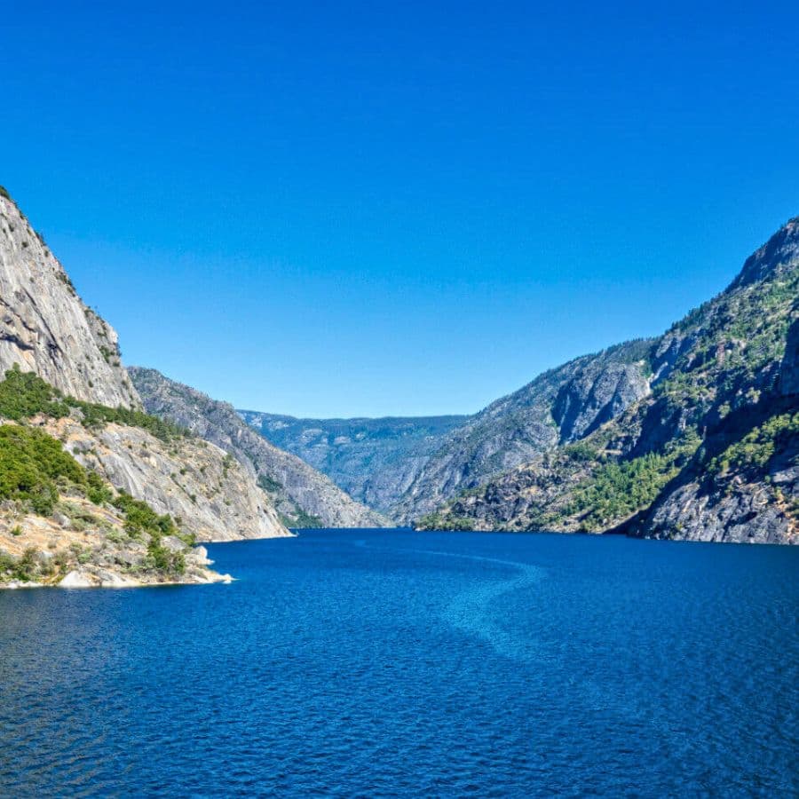 A serene lake surrounded by steep, rocky cliffs under a clear blue sky.