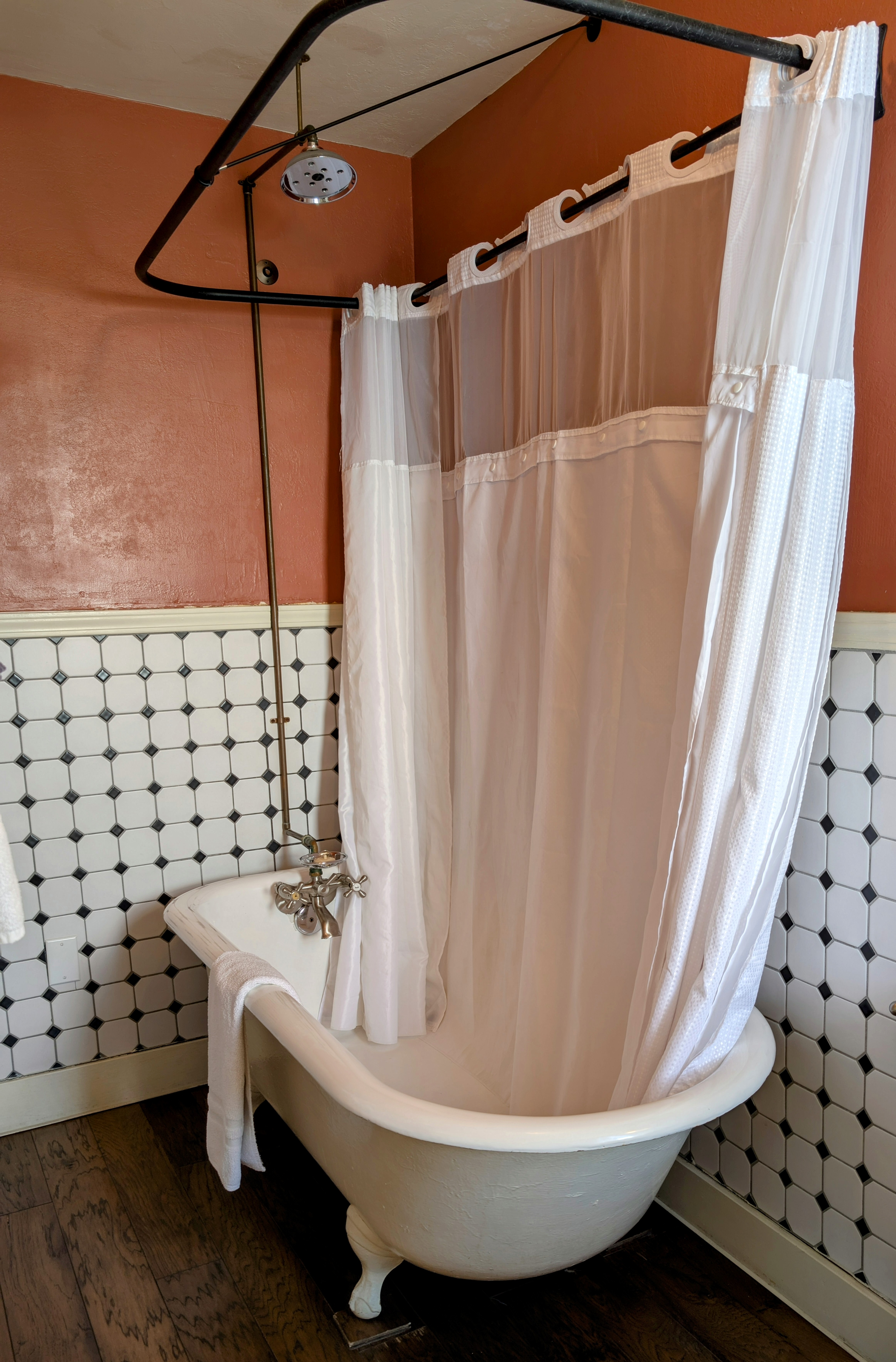 A vintage claw-foot bathtub with a shower conversion, set against rich red walls and white wainscoting with a black-square pattern.