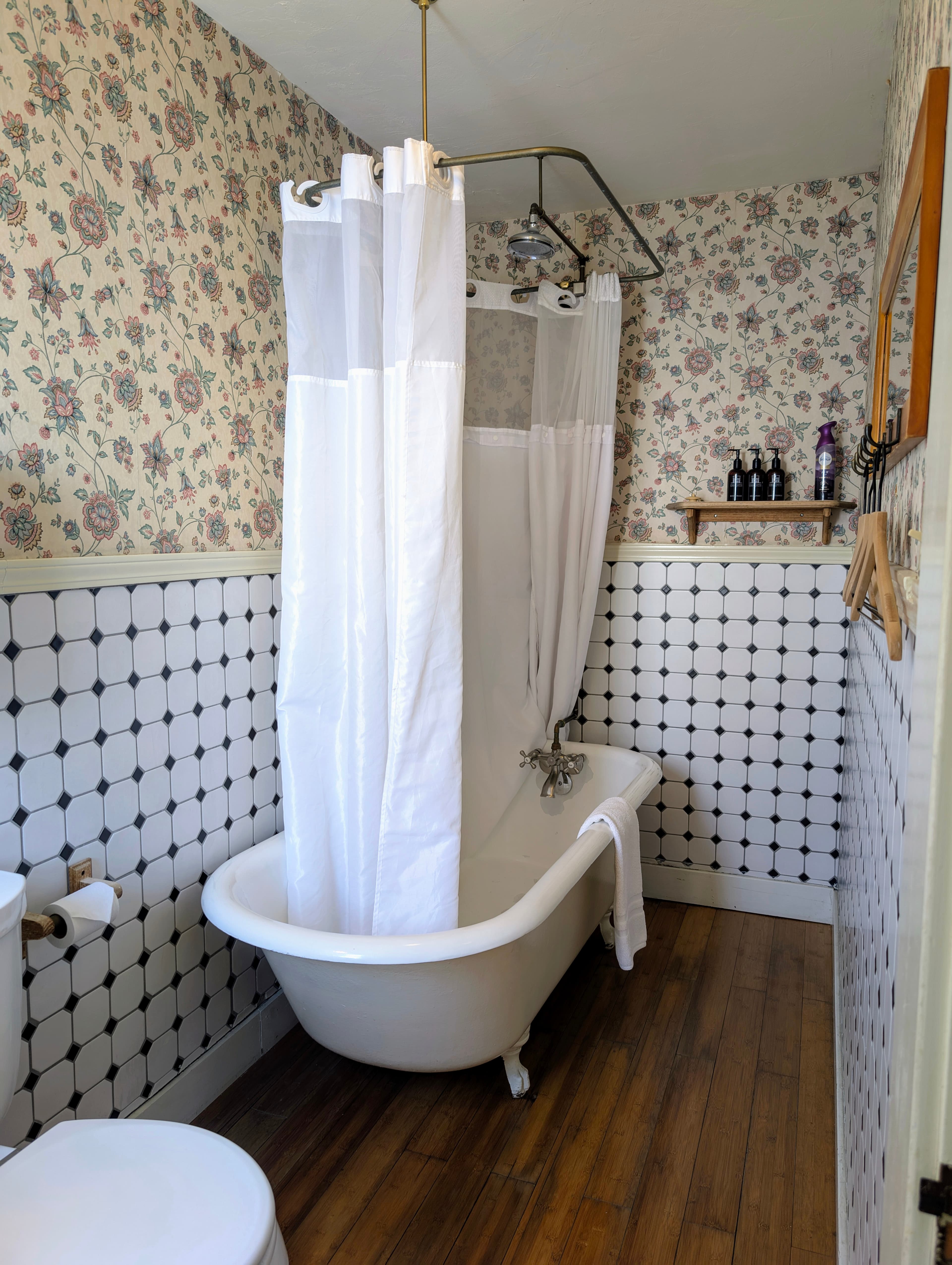 A cozy bathroom featuring a white claw-foot bathtub with a shower curtain. The walls have a mix of floral wallpaper and checkered tiles.