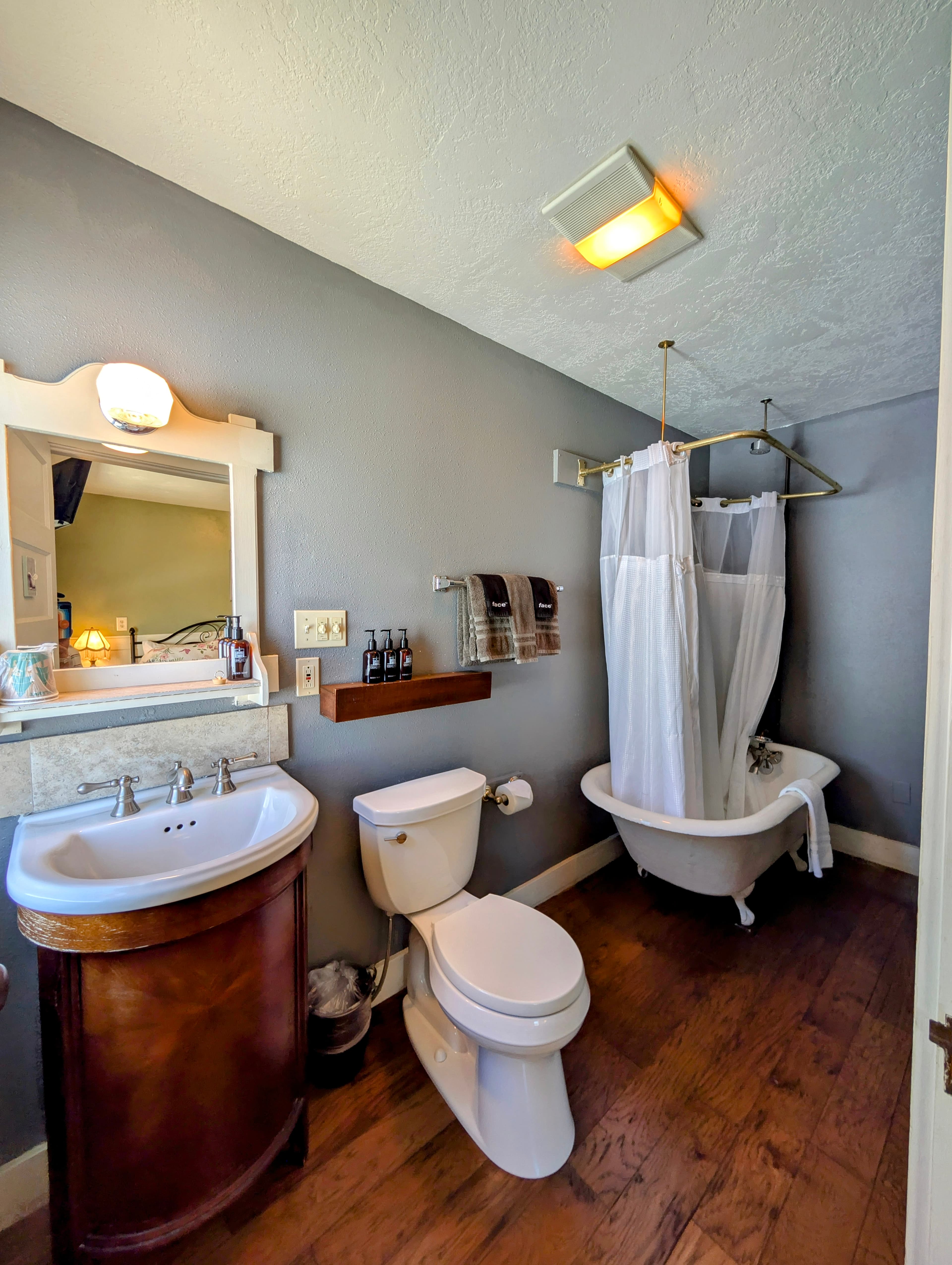 A small bathroom with gray walls, a claw-foot tub with a shower curtain, a toilet, and a sink with a dark wood vanity.