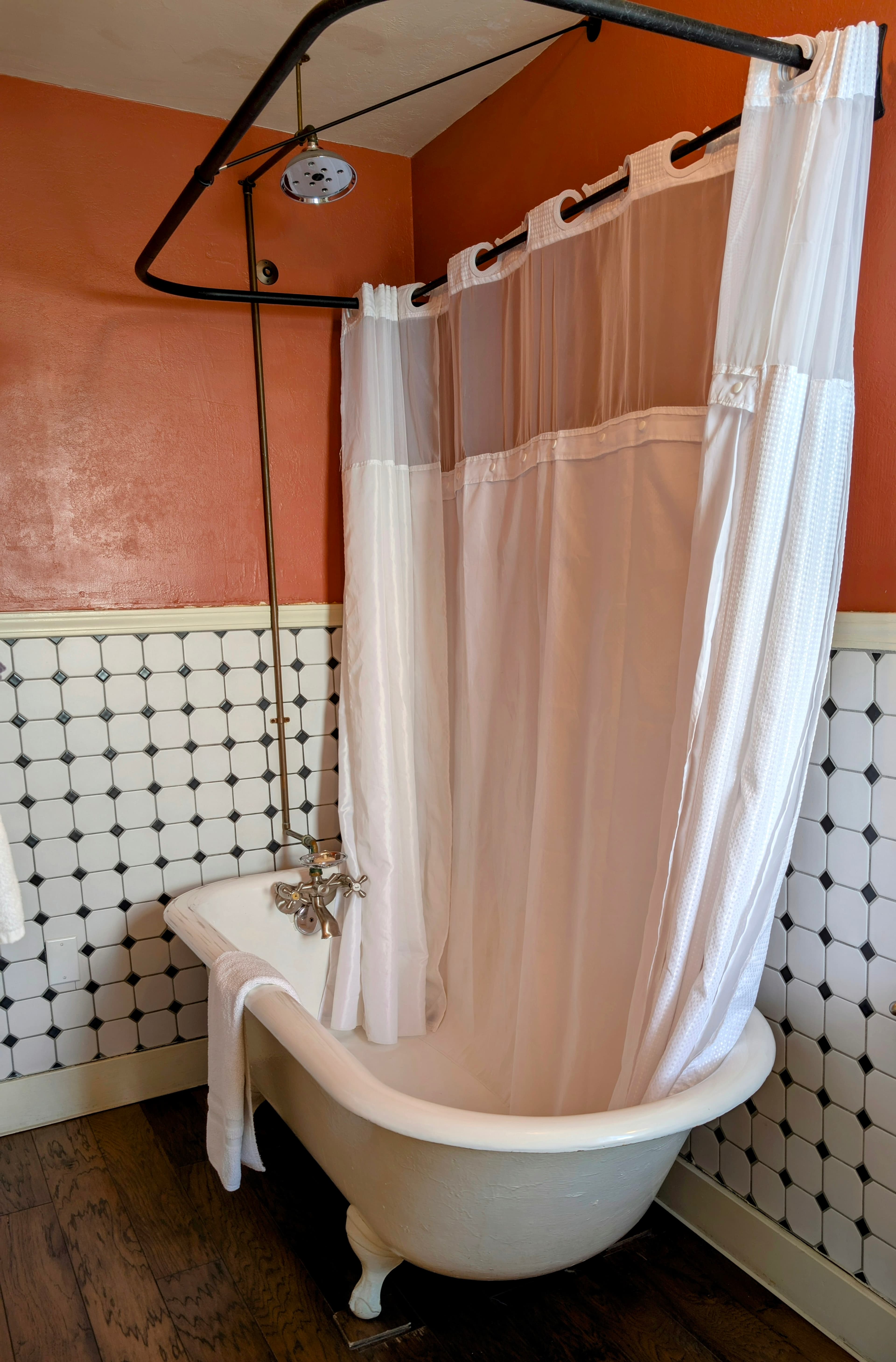 A vintage claw-foot bathtub with a shower conversion, set against rich red walls and white wainscoting with a black-square pattern.