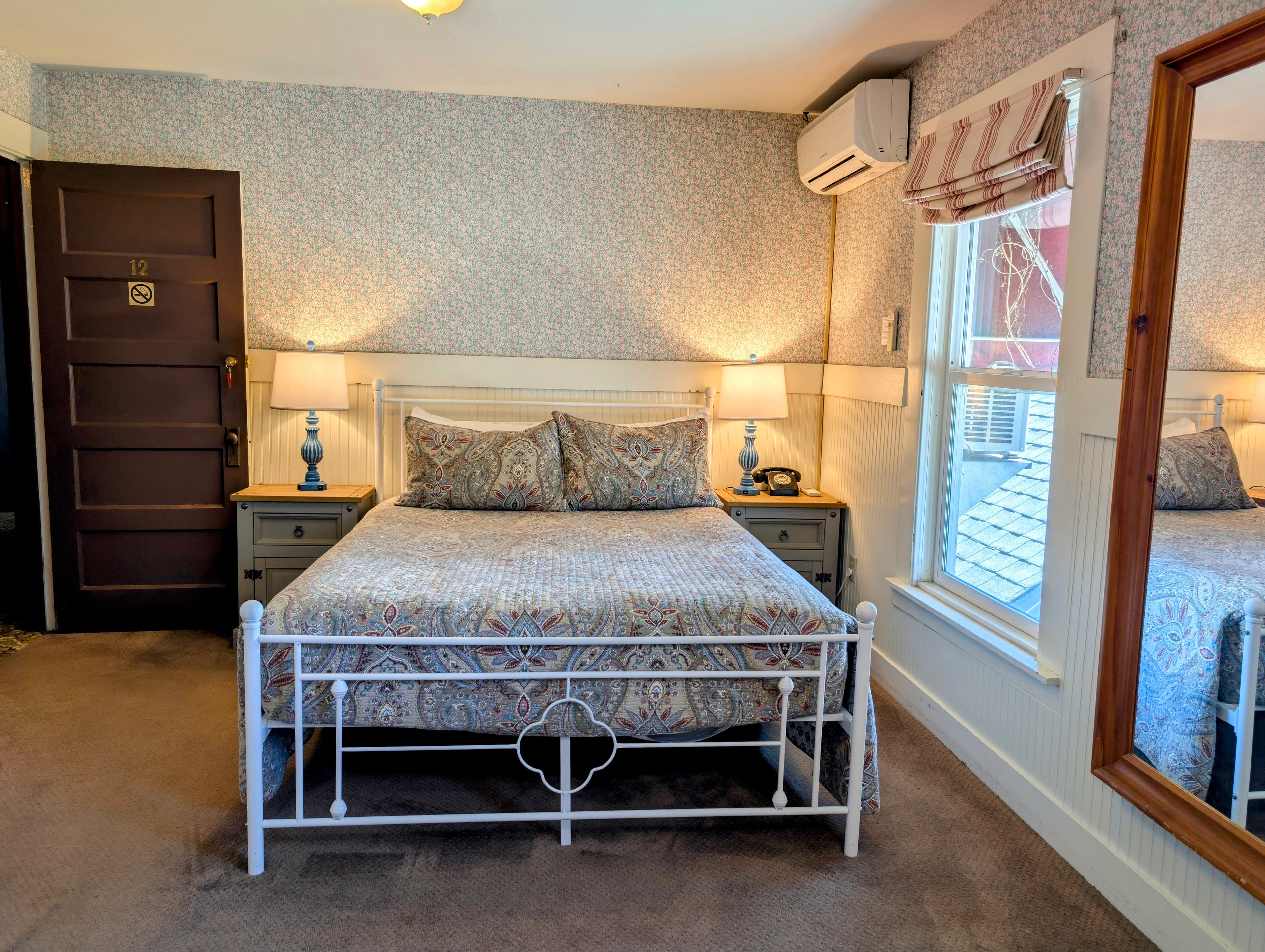 A romantic hotel room featuring a queen bed with patterned bedding, two blue lamps on matching nightstands, and patterned wallpaper.