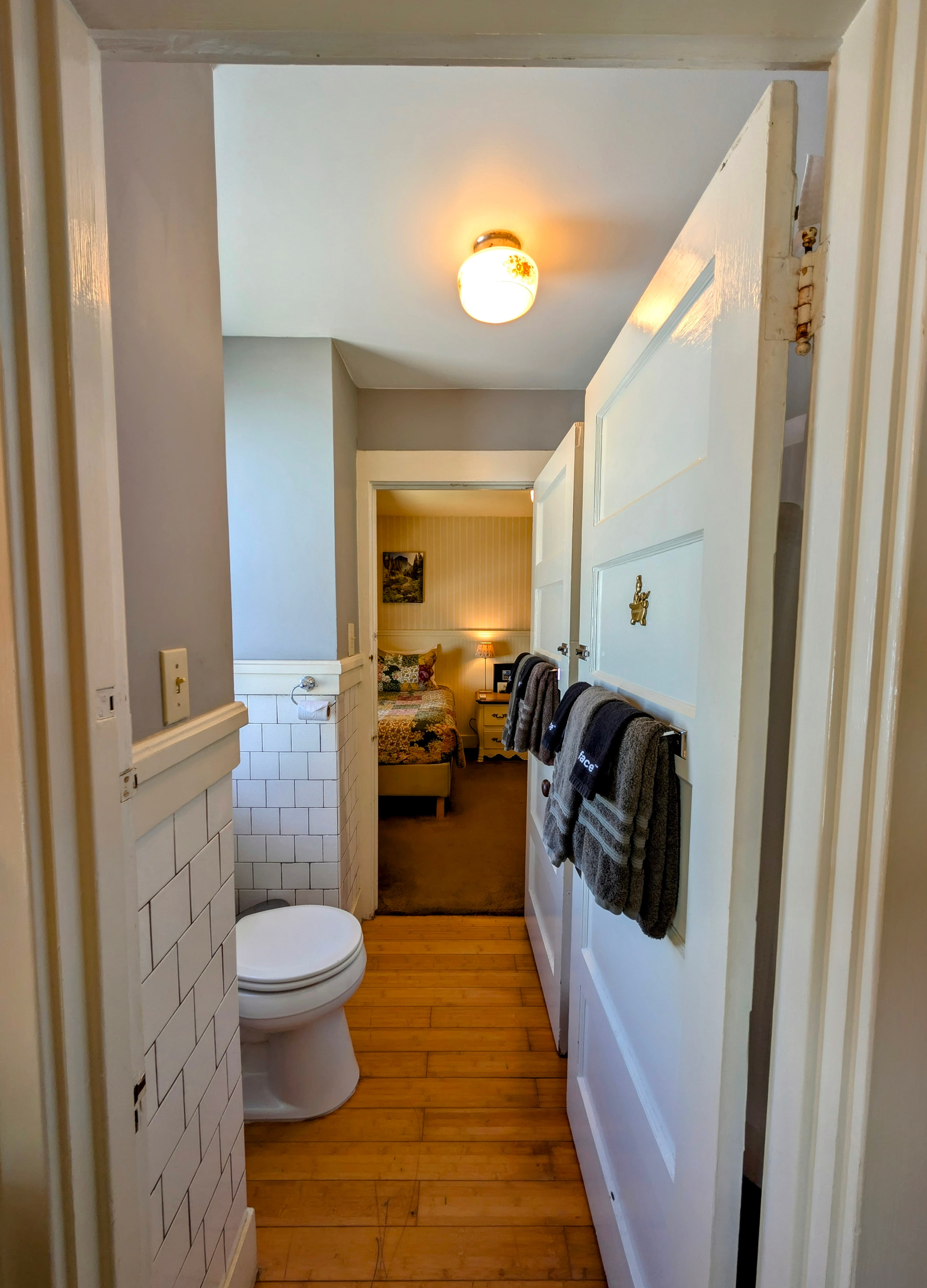 A connecting bathroom with a toilet and white wainscoting, featuring two doors that lead to the twin-bed room (Room 1) and the queen-bed room (Room 3).