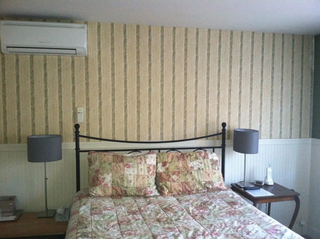 A cozy bedroom featuring a floral bedspread, two lamps, and striped wallpaper.