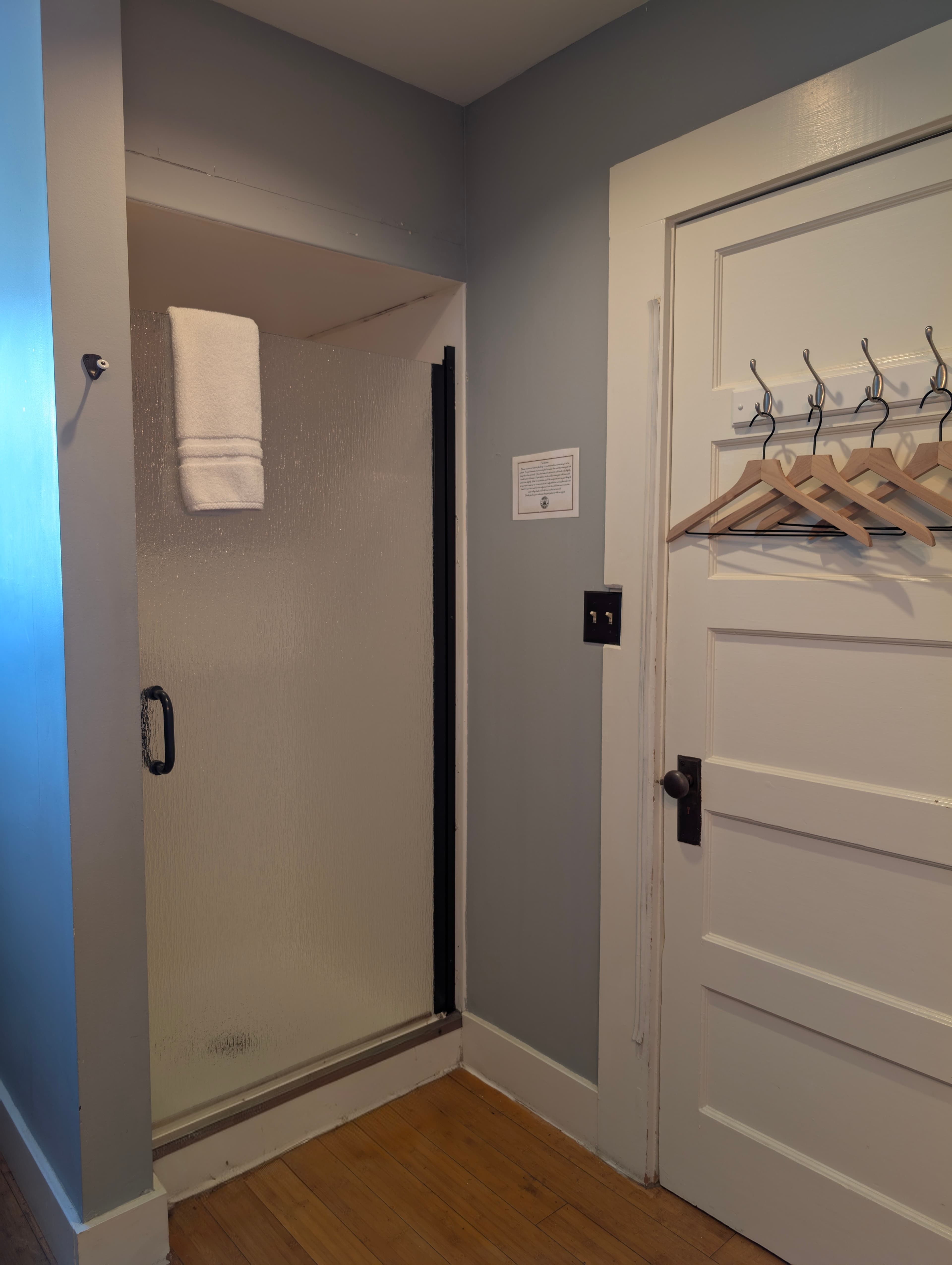 A shower stall with a towel hanging nearby and a door with coat hangers.