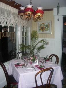 A elegantly set dining table with a white tablecloth, surrounded by wooden chairs and decorated with flowers, under a decorative chandelier.