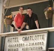 Two individuals pose together on a balcony in front of the Hotel Charlotte sign.