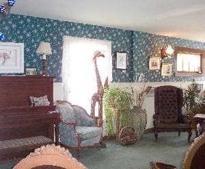 A cozy living room with vintage furniture, wallpaper, and plants.