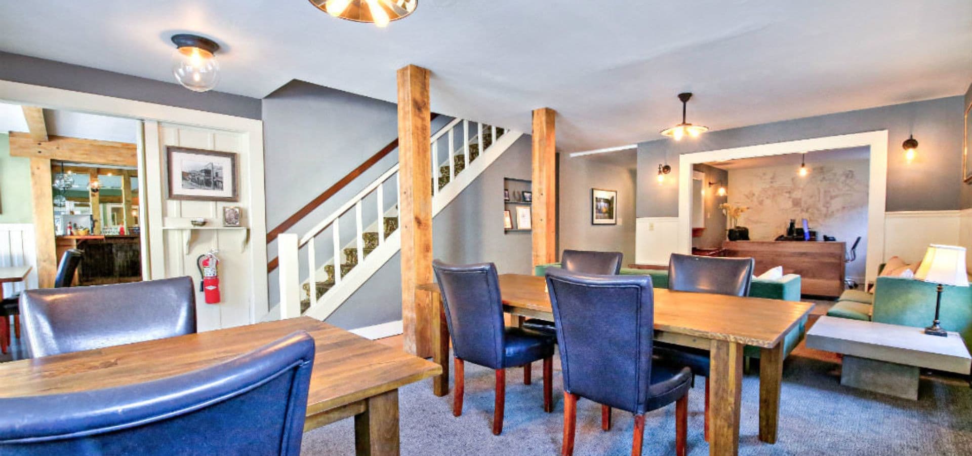 A cozy dining area with wooden tables, upholstered chairs, and a staircase in a modern setting.