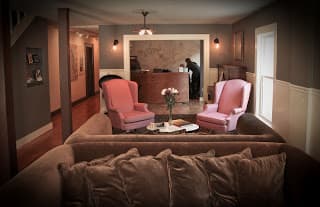 Cozy living room with two pink chairs, a brown sofa, and a reception area in the background.