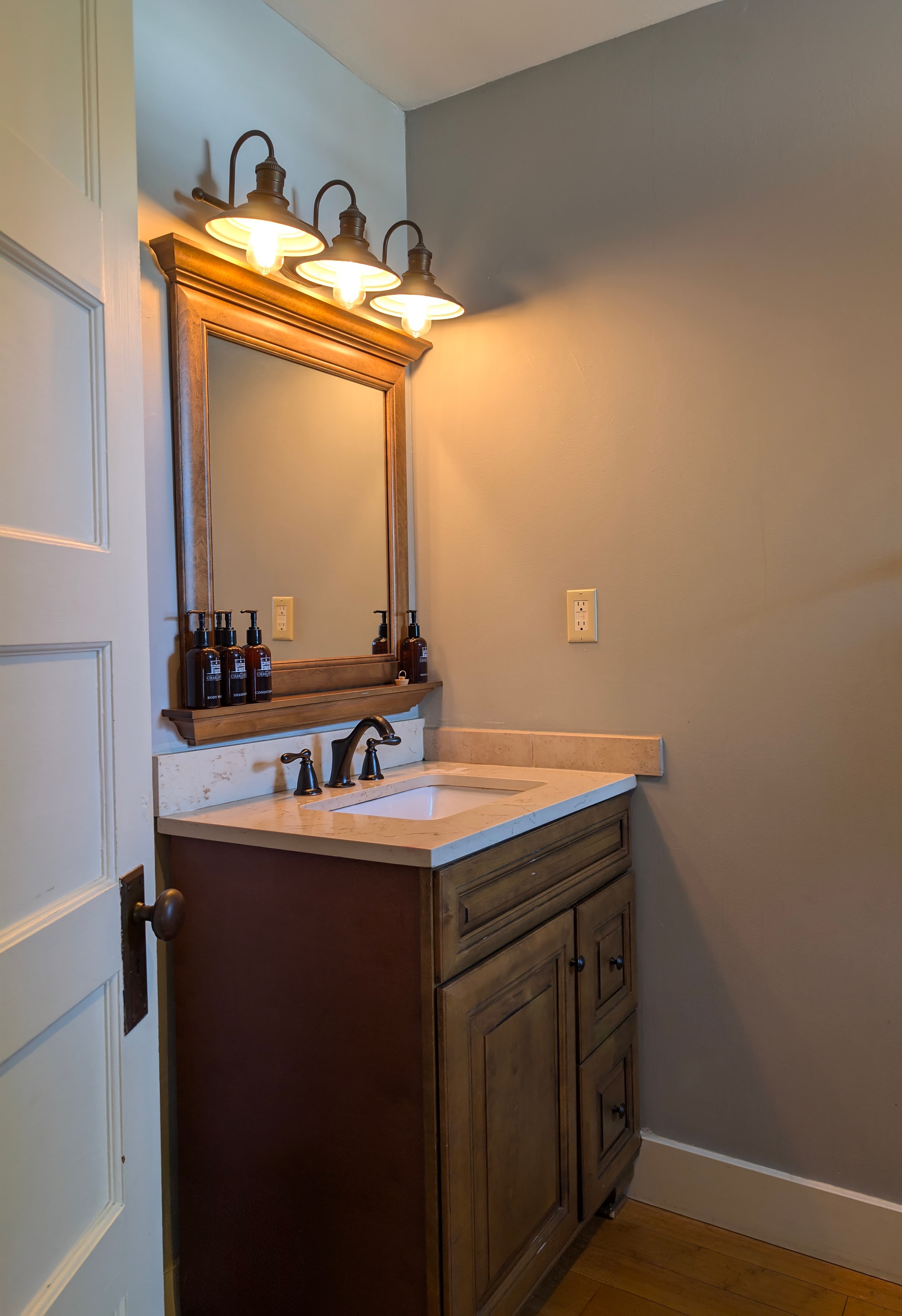 A small bathroom featuring a wooden vanity, sink, and illuminated mirror.