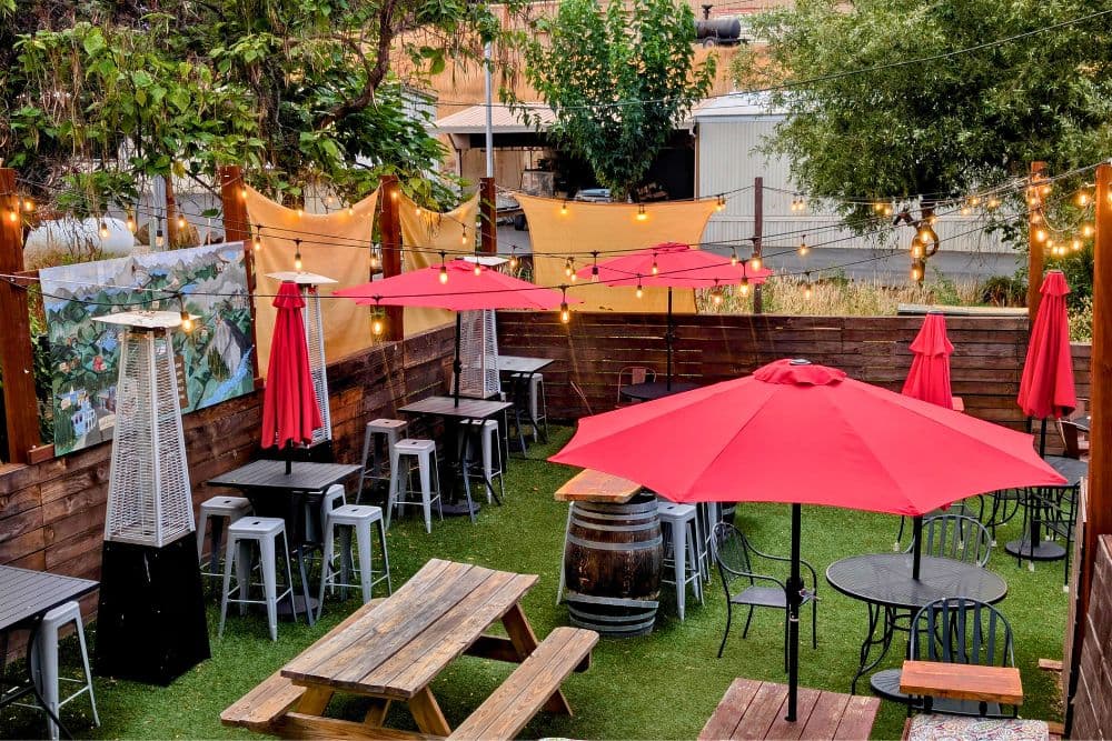 An outdoor dining area featuring wooden tables, red umbrellas, and string lights.