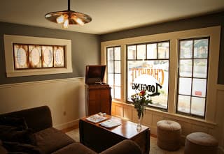 A cozy living room featuring a brown couch, coffee table, and large windows with a 'Charriott Tasting' sign.