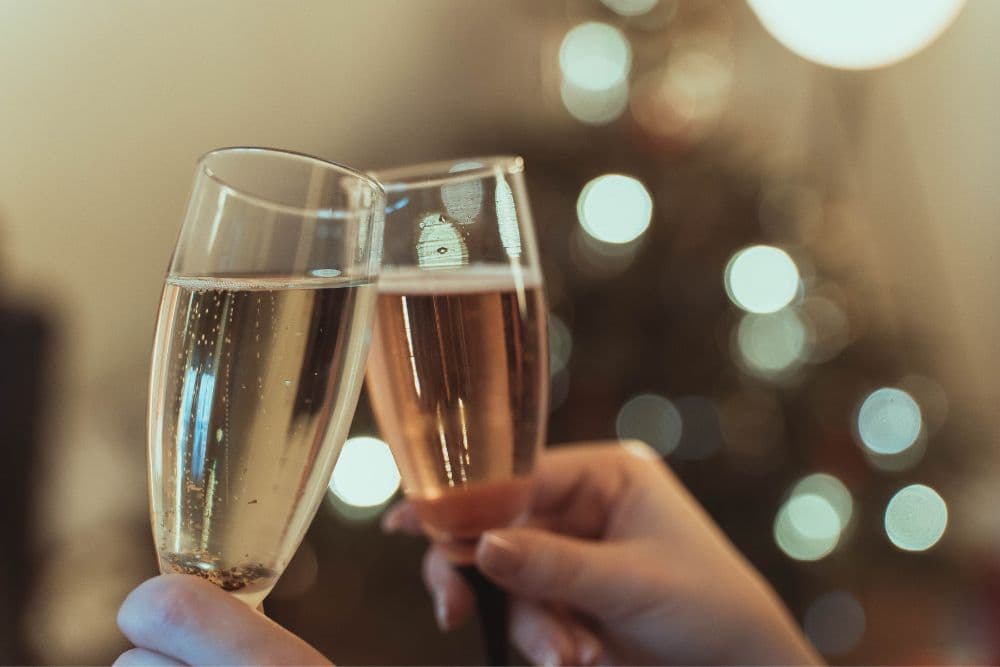 Two glasses of sparkling wine clinking together, with a softly blurred background of holiday lights.