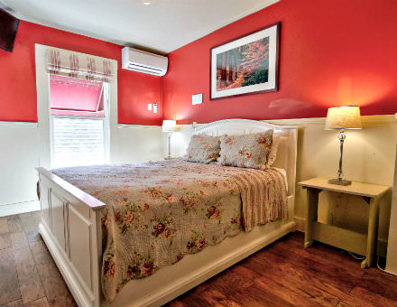 Red guest bedroom with white chair rail paneling, hardwood floors, and lovely floral bedding