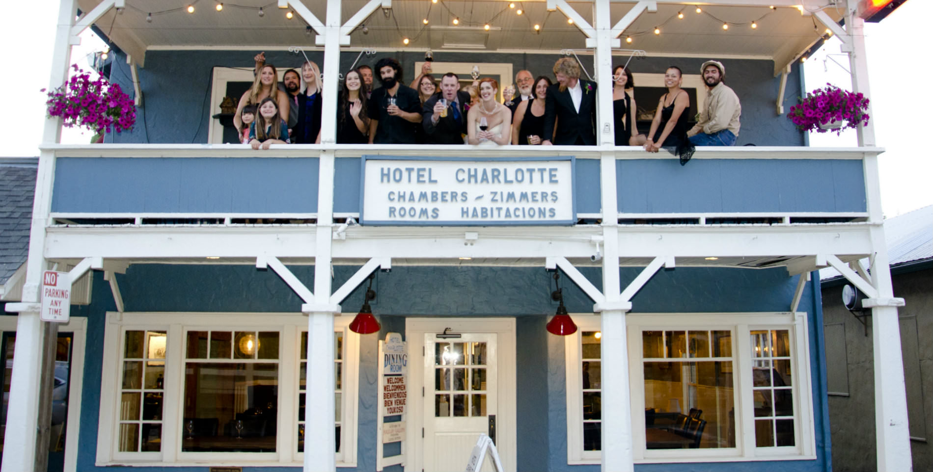 A large wedding party outside on the balcony of Hotel Charlotte, a blue and white building