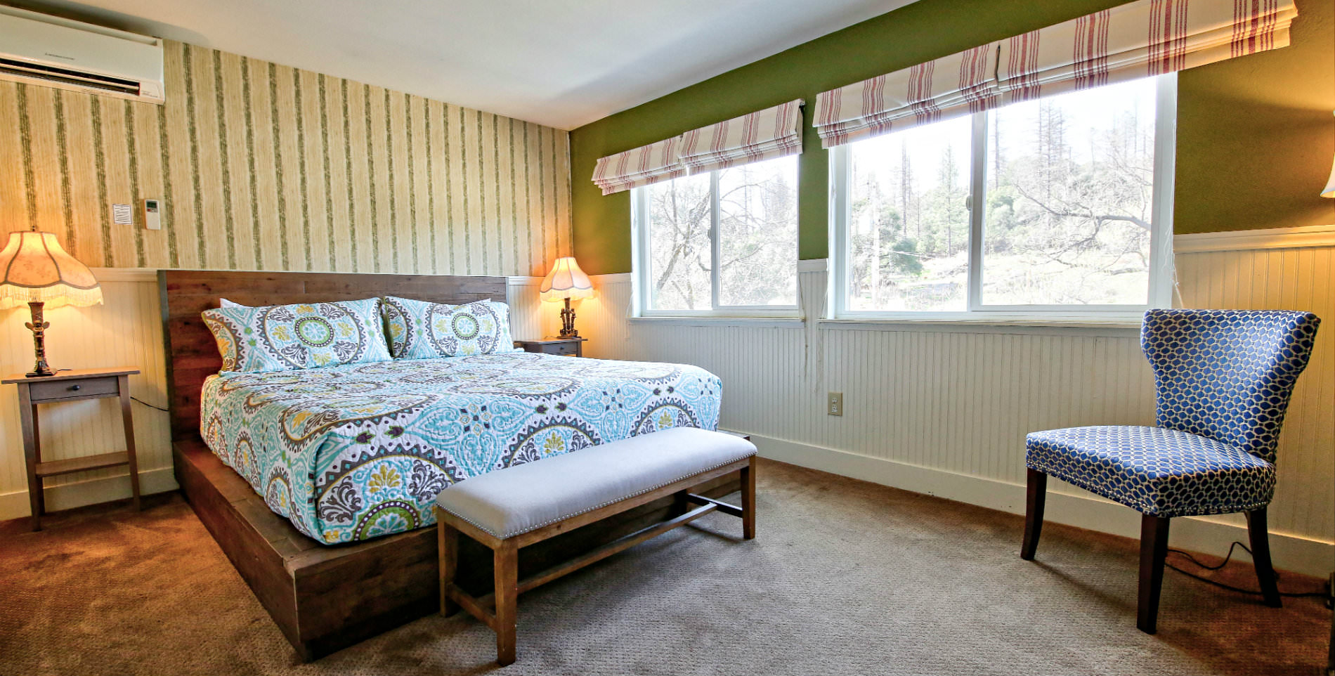 Guest bedroom with soft carpeted floors, turquoise and brown paisley bedding, and two large windows