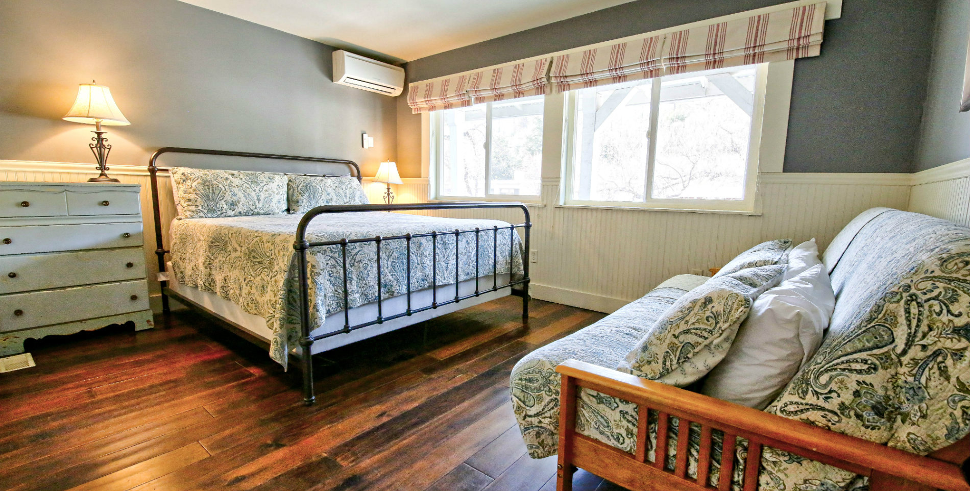 Hardwood guest bedroom with grey walls, green paisley bedding, and a futon