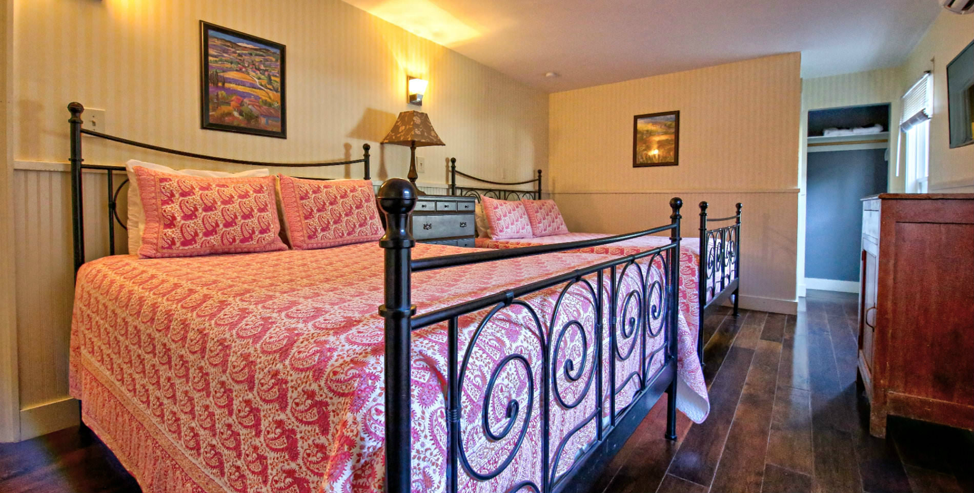 Guest room with cream striped wallpaper, two beds with bright pink bedding, hardwood floors