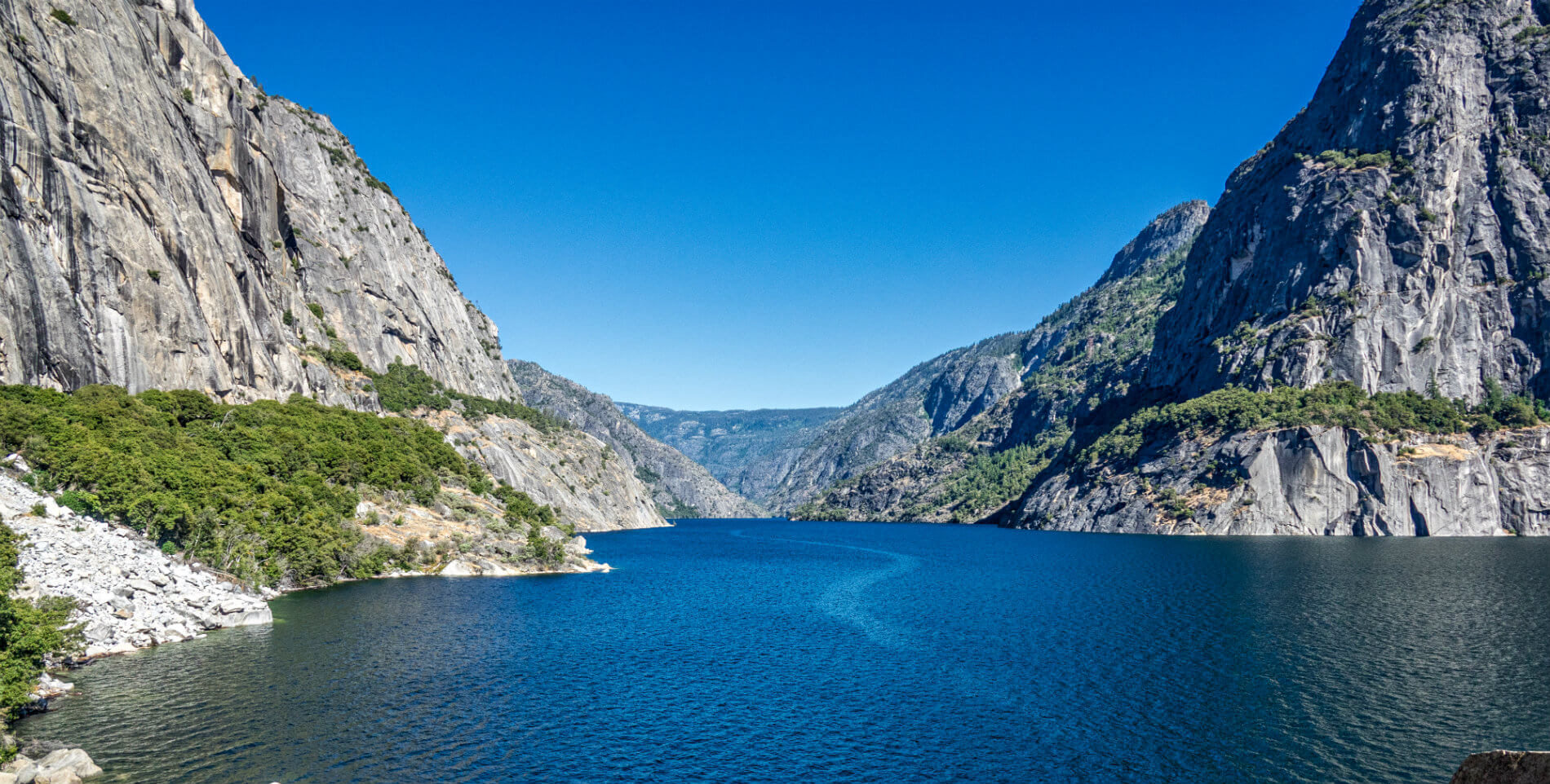 beatiful crystal blue lake surrounded by rocky mountains on each side and moutain in distance with blue skies with no clouds