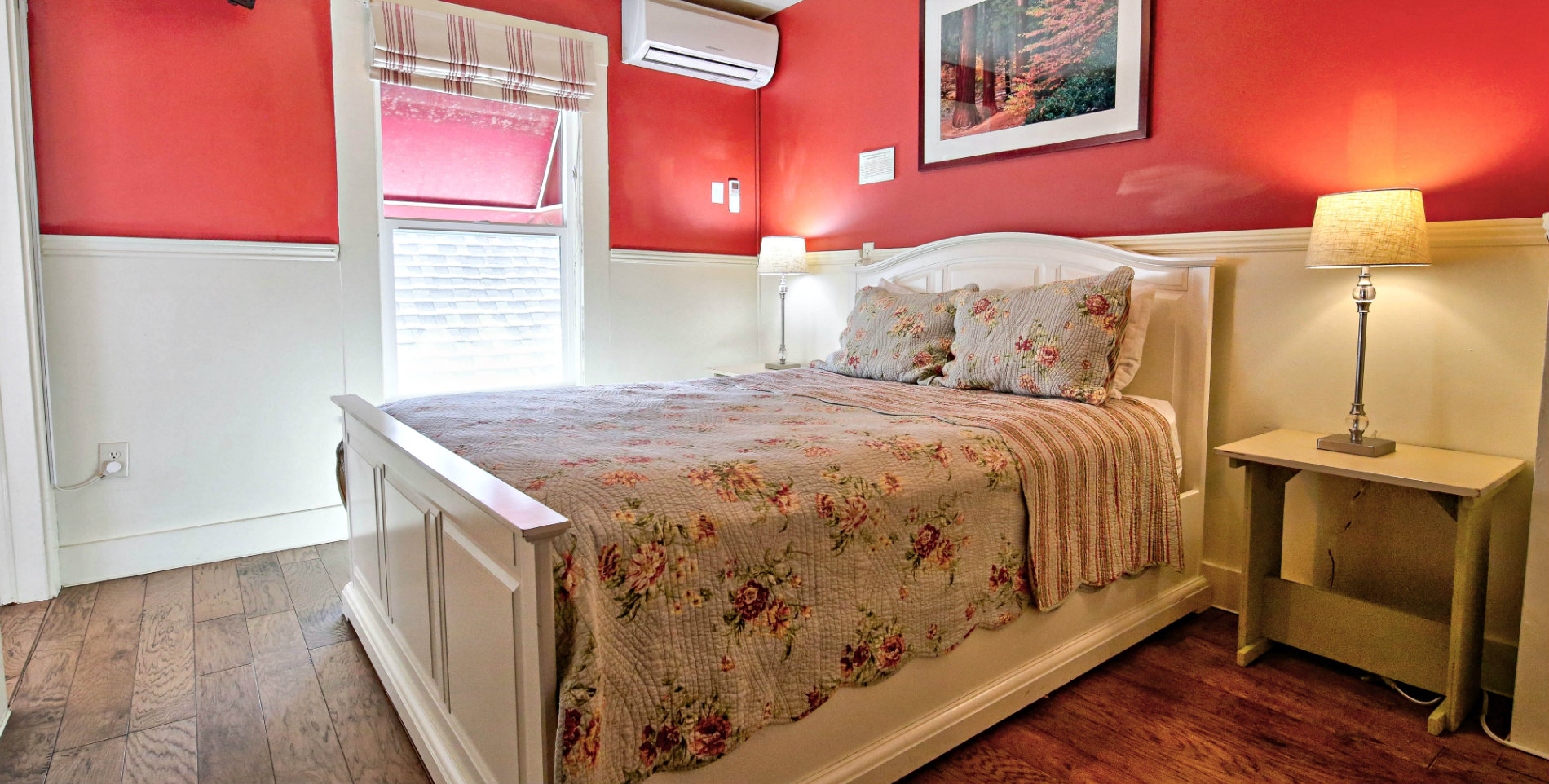 Red guest bedroom with white chair rail paneling, hardwood floors, and lovely floral bedding