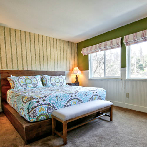Guest bedroom with soft carpeted floors, turquoise and brown paisley bedding, and two large windows