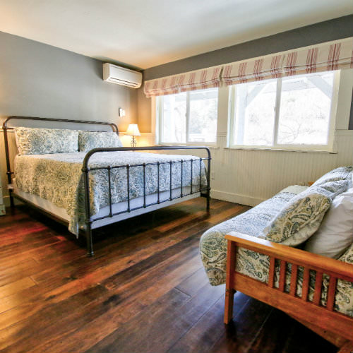 Hardwood guest bedroom with grey walls, green paisley bedding, and a futon