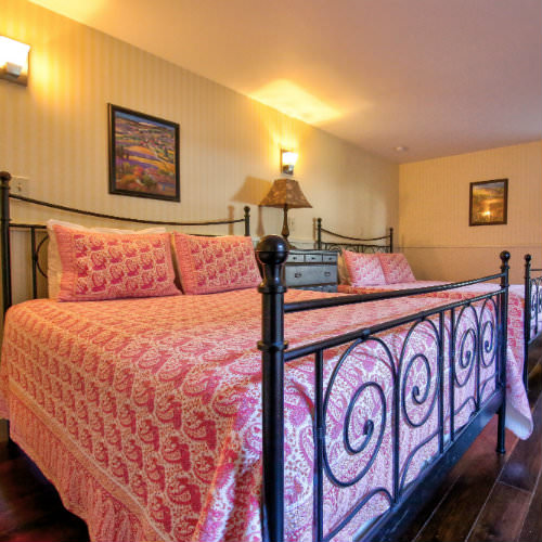 Guest room with cream striped wallpaper, two beds with bright pink bedding, hardwood floors