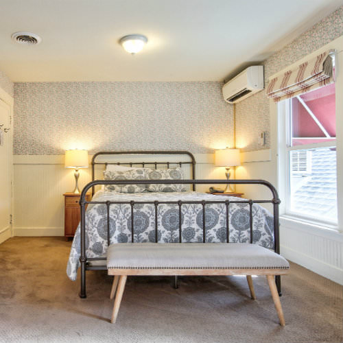 Carpeted guest room with grey and white bedding, double night stands, and white chair rail side paneling