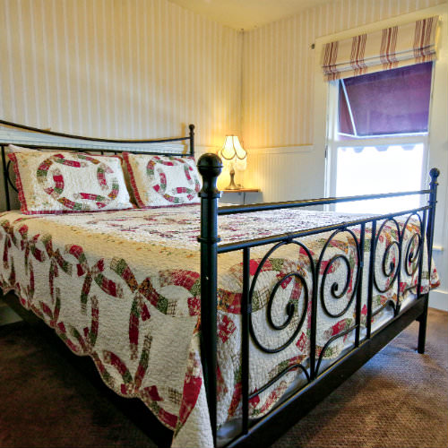 Brown carpeted guest bedroom with red and green patterned bedding, striped wallpaper, and bedside lamp