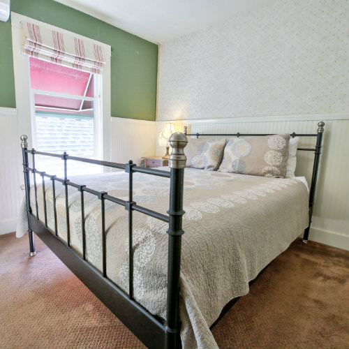 Green and white guest bedroom with brown carpeted floors, tan bedding, and a side table with reading lamp