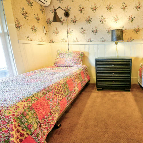 Guest bedroom with floral wallpaper, carpeted, with two pink quilted beds with a nightstand in between