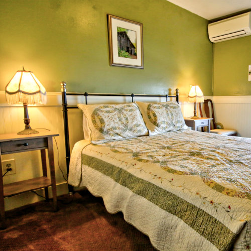 Green guest bedroom with brown carpeted floors, two wooden nightstands with reading lamps