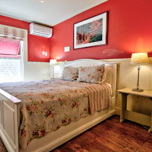 Red guest bedroom with white chair rail paneling, hardwood floors, and lovely floral bedding