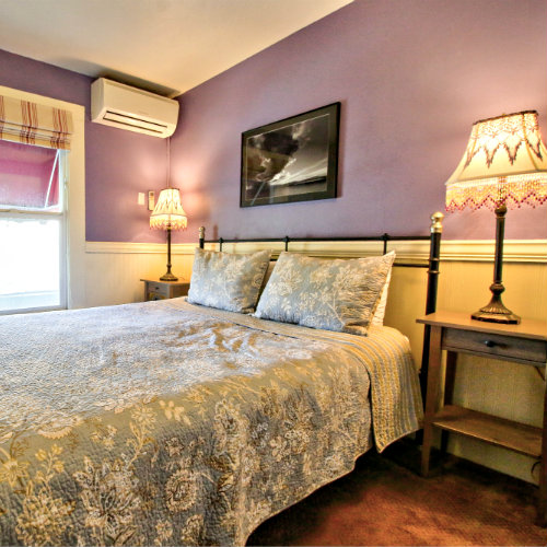 Carpeted guest room with purple walls, green floral bedding, and two nightstands with reading lamps