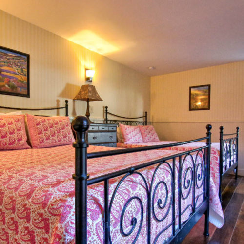 Side by side queen black cast iron beds with soft pink linens , soft cream colored walls on wood floor.