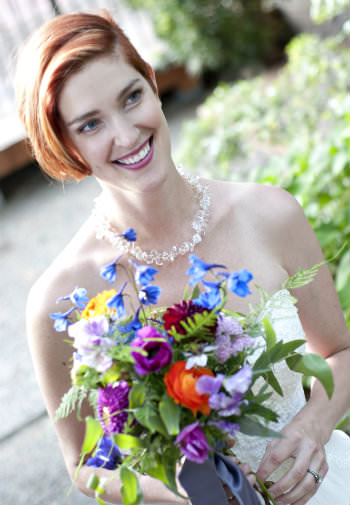 Beautiful smiling woman in a crisp white wedding gown holding a bouquet of multicolored wildflowers