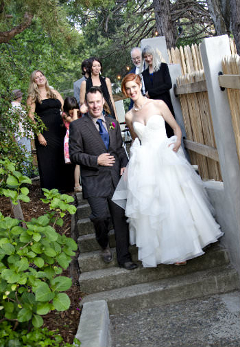 A woman with short red hair in a wedding gown surrounded by people all walking down a stone stairway