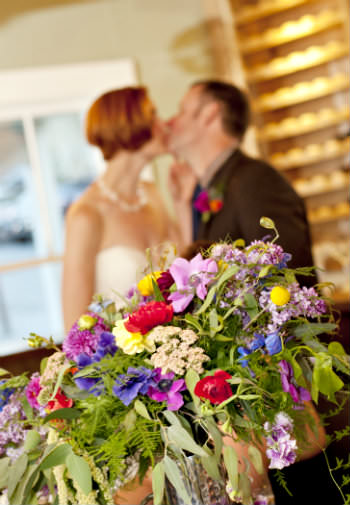 A newly wed couple kissing in a blurred background with a bouquet of wild flowers in the foreground