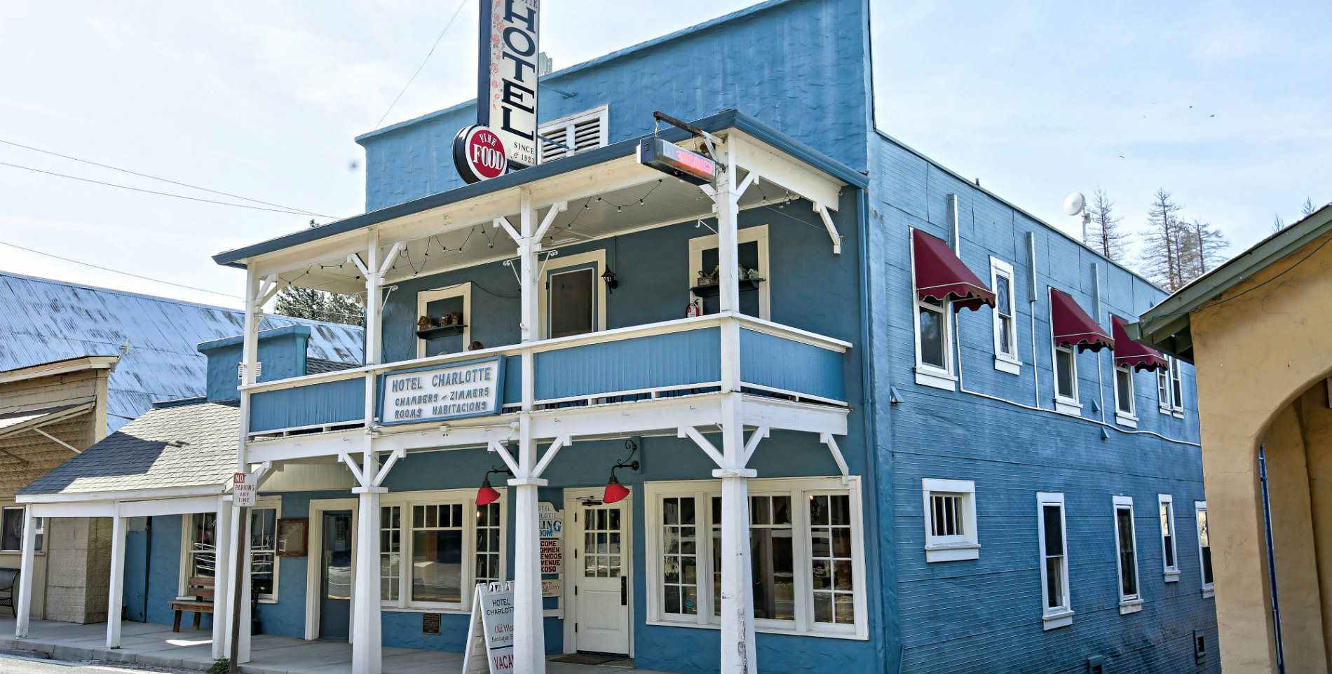 street view of the two story sky blue painted hotel with second story balcony with white trim and burgundy window awnings on the side